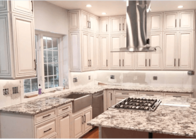 Remodeled kitchen with granite countertops, custom white cabinets, farmhouse sink, stainless steel cooktop, and overhead vent hood.