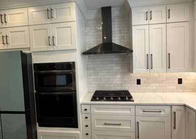 Renovated kitchen featuring a new cooktop, stainless steel hood, double oven, subway tile backsplash, quartz countertops, and white shaker cabinets.