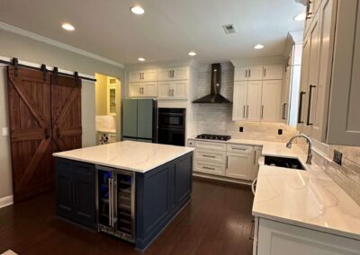 Renovated kitchen with navy blue island, built-in wine cooler, quartz countertops, subway tile backsplash, white shaker cabinets, wooden barn door, and a replaced cooktop