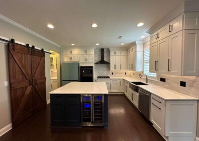 Modern kitchen remodel with white shaker cabinets, quartz countertops, navy blue island with a wine cooler, subway tile backsplash, and a wooden barn door.