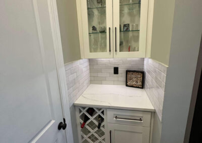 Pantry nook with white shaker cabinets, a built-in wine rack, glass-front display cabinets, quartz countertop, and white subway tile backsplash.