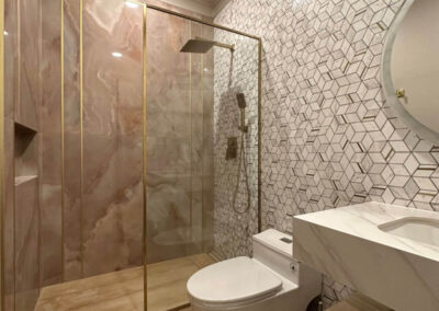 Bathroom with a marble shower with gold trim, geometric tile accent wall, custom vanity with quartz countertop, and frameless glass door.