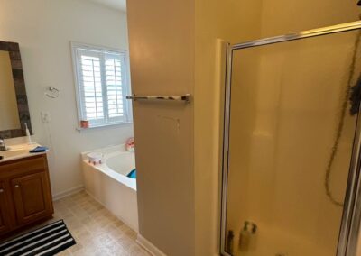 A bathroom in the initial stages of a remodel, with plans to replace the old shower enclosure with a modern walk-in design, refresh the bathtub and flooring, and update lighting and fixtures for a functional, clean, and stylish space.