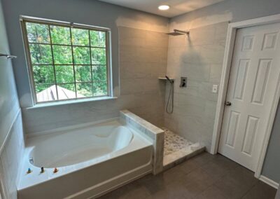 Bathroom with a soaking tub, walk-in shower with large-format tiles and pebble stone floor, and a window bringing in natural light.