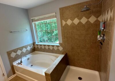 Bathroom with a soaking tub, tiled surround, walk-in shower with decorative tile accents, and a large window providing natural light.