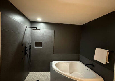 Bathroom with a walk-in shower featuring black fixtures, a jacuzzi tub, dark accent walls, and neutral tile flooring.