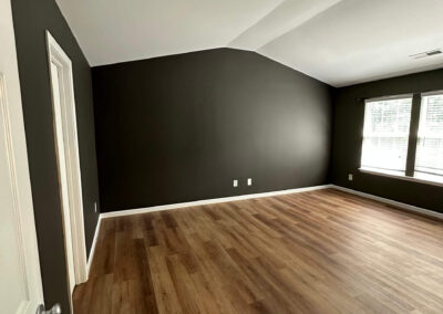 Remodeled room with dark accent walls, hardwood flooring, vaulted ceiling, and large windows for natural light.