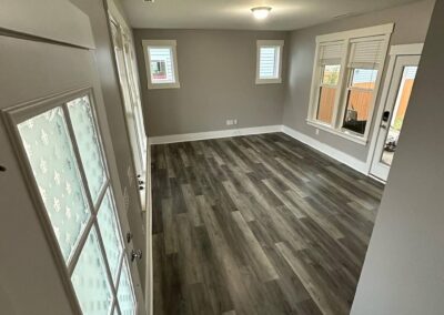 A room with newly installed luxury vinyl plank flooring in gray, freshly painted walls, white trim, large windows, and a glass-paned door.