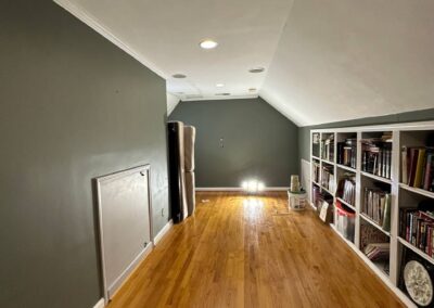 A room with newly refinished hardwood flooring, deep gray painted walls, recessed lighting, and built-in bookshelves.