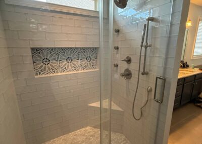 Walk-in shower with glass sliding door, white subway tiles, and decorative accent panel
