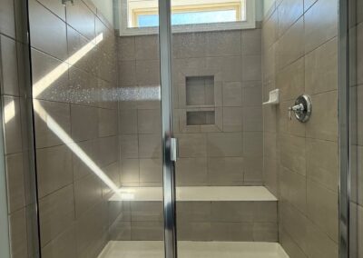 Walk-in shower with beige wall tiles, glass door, and built-in bench