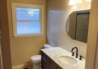 Bathroom with wood vanity, marble countertop, modern black faucet, and round mirror