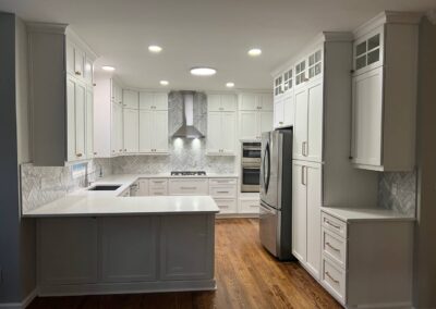 Modern white kitchen with shaker cabinets, herringbone backsplash, and stainless steel appliances