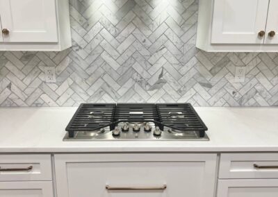 Stainless steel range hood above gas cooktop with white shaker cabinets and herringbone backsplash