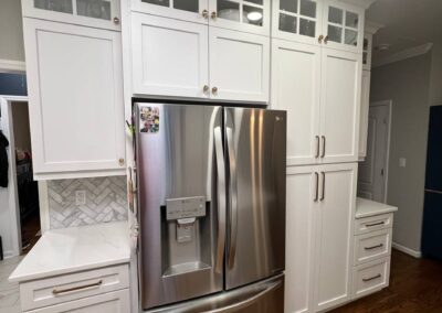 Stainless steel refrigerator surrounded by custom white cabinets with glass inserts