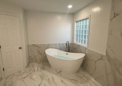 Luxury bathroom with freestanding tub, marble tile flooring, and geometric rug.