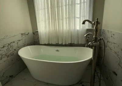 Freestanding soaking tub with marble tile floor and chrome faucet in a modern bathroom.
