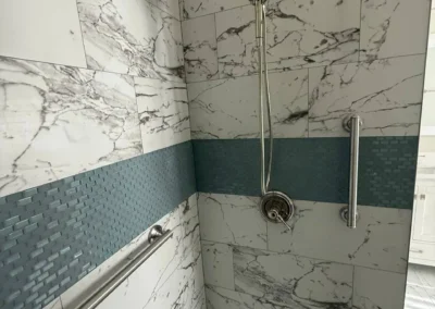 Walk-in shower with marble wall tiles, blue mosaic accent strip, and dual showerheads.