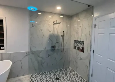 Walk-in shower with marble walls, geometric floor tiles, and glass enclosure.