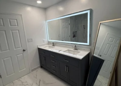 Modern bathroom with dark double vanity, LED mirror, and marble floor tiles.