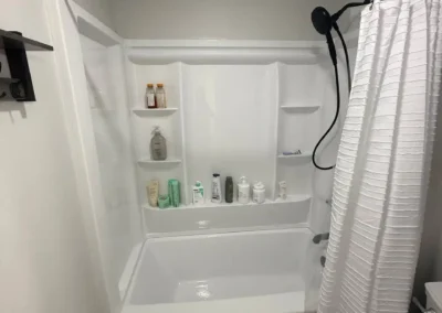 Small bathroom with white bathtub and shower combo, black showerhead, and gray patterned floor.
