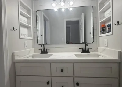 Modern bathroom with white double vanity, black faucets, and large framed mirror.