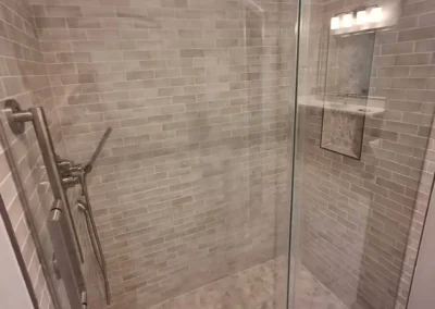 Walk-in shower with glass door, beige subway tiles, and rainfall showerhead.
