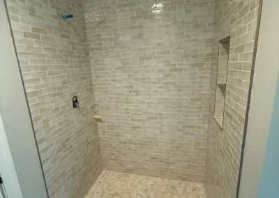 Walk-in shower with beige subway tiles and built-in corner shelf.