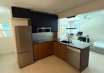 Compact modern kitchen with wood cabinets, black countertops, and stainless steel appliances.