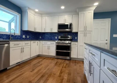 Renovated kitchen with white cabinets, stainless steel appliances, and blue mosaic backsplash.