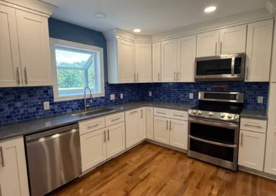 Renovated kitchen with white cabinets, stainless steel appliances, and blue mosaic backsplash.