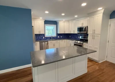 Modern kitchen remodel with white cabinets, blue tile backsplash, and central island.