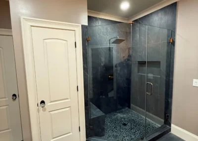 Custom glass walk in shower installation with dark tile walls